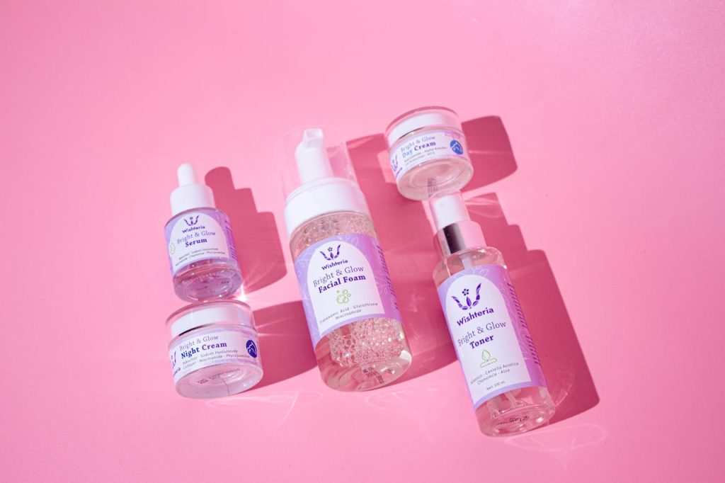 Flat lay of various skincare products on a vibrant pink background.
